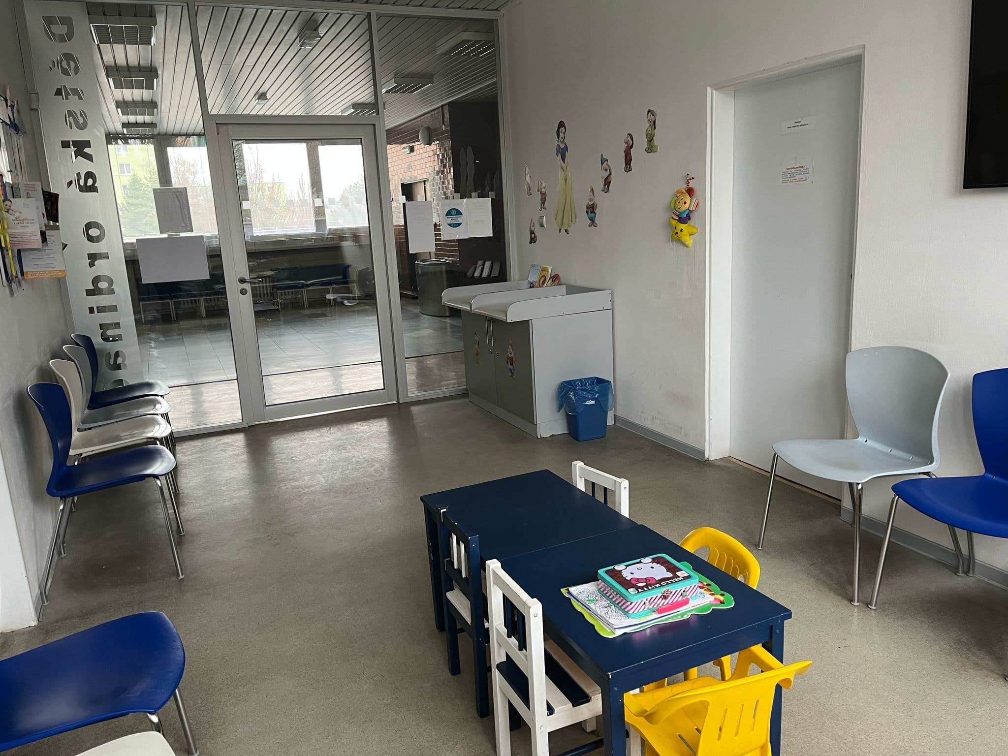 Čekárna dětské ordinace s modrými a šedými židlemi, dětským stolečkem a židličkami.