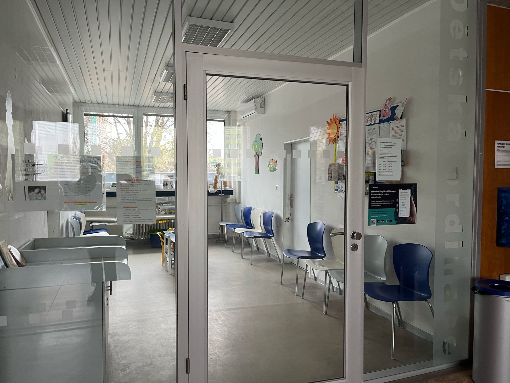 Vchod do čekárny dětské ordinace s modrými a bílými židlemi podél stěny.